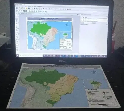Foto enviada pelo aluno Ruan no grupo: o mapa dos biomas do Brasil impresso, ao lado do projeto aberto no QGIS